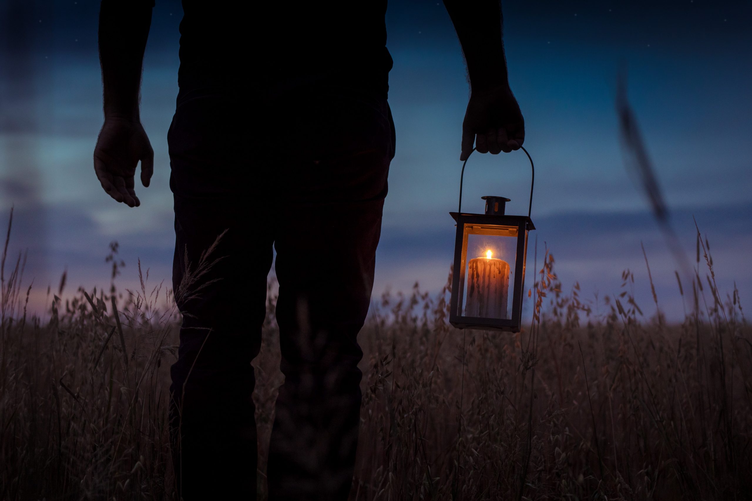 Closeup of man holding lantern, walking in a field at night